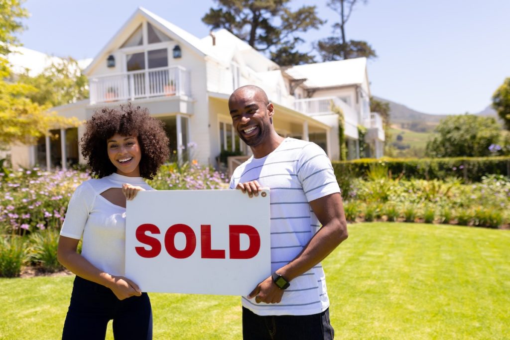 Young couple holding "sold" sign in front yard